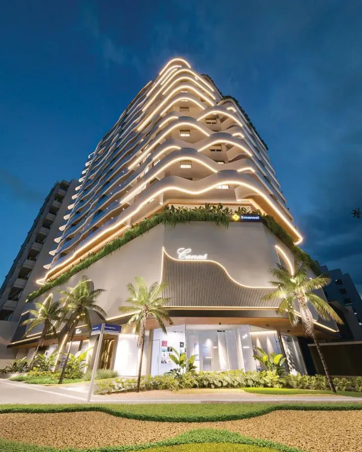 Esquina do Canaã Residence à noite, com as sacadas curvas iluminadas e a base com o letreiro do prédio