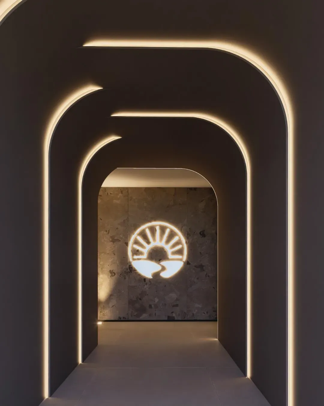 Túnel de acesso do Canaã Residence em arcos com luz indireta e o símbolo do prédio na parede ao fundo