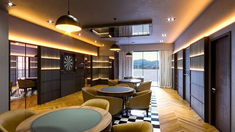 Sala de jogos do Carmel Residence com mesas de carteado, alvo de dardos e iluminação indireta