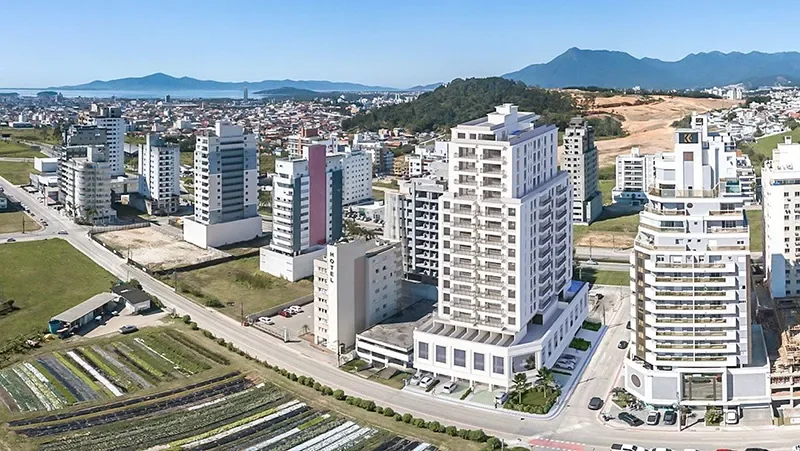 Vista aérea do Carmel Residence entre os prédios da Pedra Branca, com os morros e a baía ao fundo