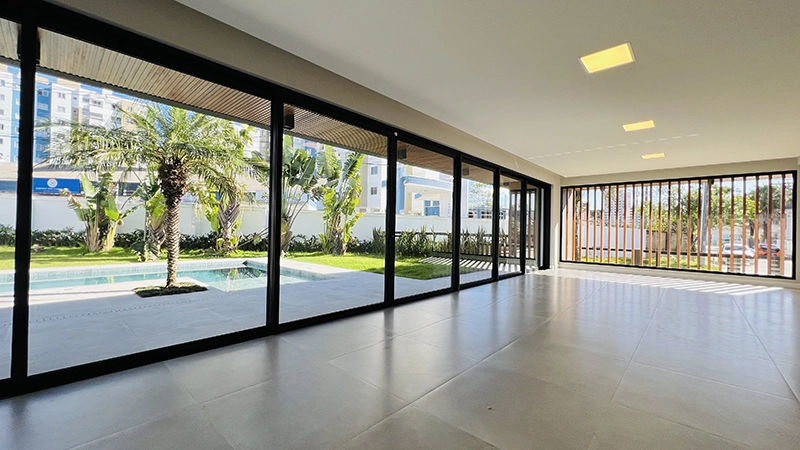 Salão envidraçado com vista para a piscina e o jardim com palmeiras, área de lazer de casa em condomínio na Pedra Branca, Palhoça/SC