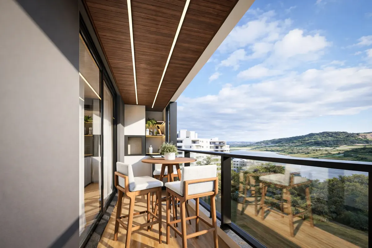 Sacada do apartamento decorado do Kairós Residence, com mesa alta, guarda-corpo de vidro e vista para o lago e os morros