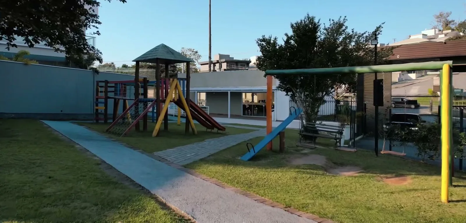 Playground de madeira colorida com escorregador e balanços no gramado do condomínio