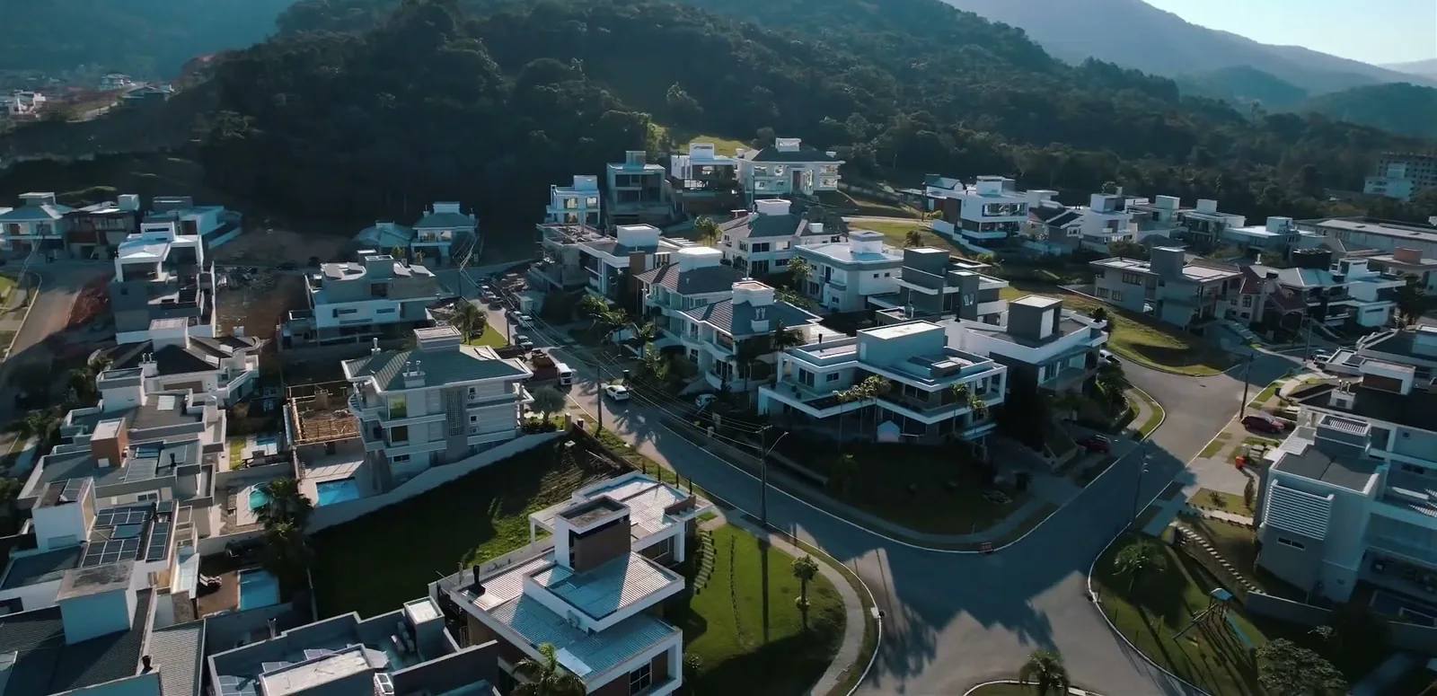 Vista aérea de casas do condomínio, com piscinas nos quintais, jardins e a mata atrás