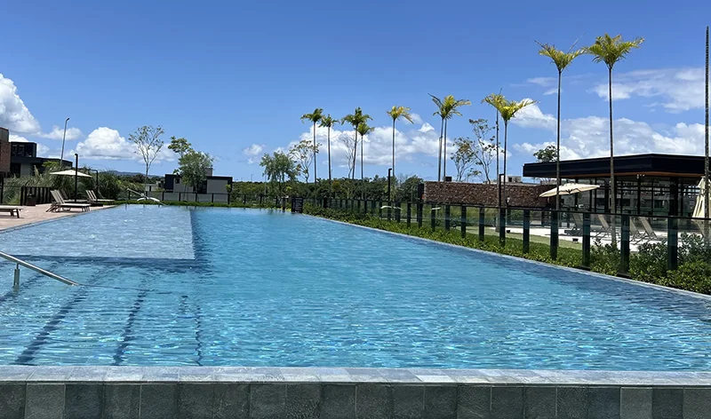 Piscina adulto com raia, palmeiras e deck com espreguiçadeiras do condomínio Reserva da Pedra em Palhoça/SC