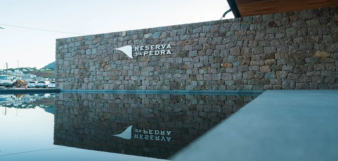 Muro de pedra com o nome Reserva da Pedra refletido no espelho d'água da entrada