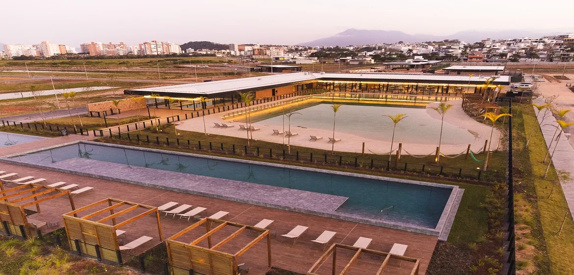Foto aérea do clube do Reserva da Pedra, com a praia artificial de areia, bangalôs e a piscina adulta ao lado